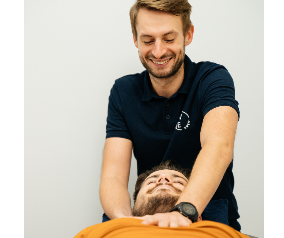 Uśmiechnięty fizjoterapeuta w trakcie pracy manualnej w obszarze szyi i klatki piersiowej u młodego, leżącego chłopaka z zarostem na twarzy.